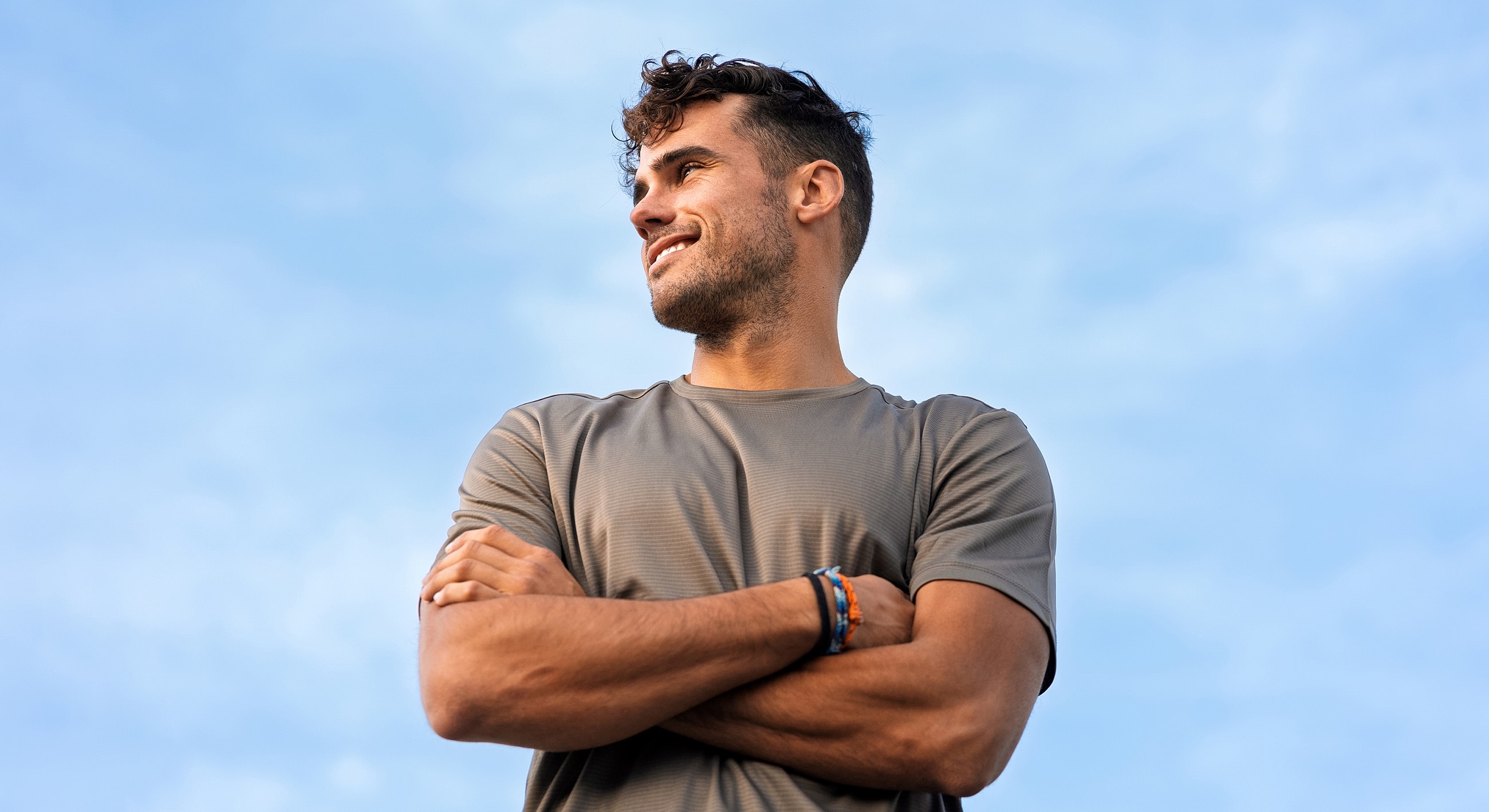 Smiling man with crossed arms against blue sky.