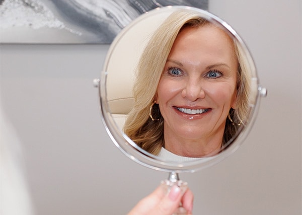 Woman smiling in mirror reflection, holding mirror.